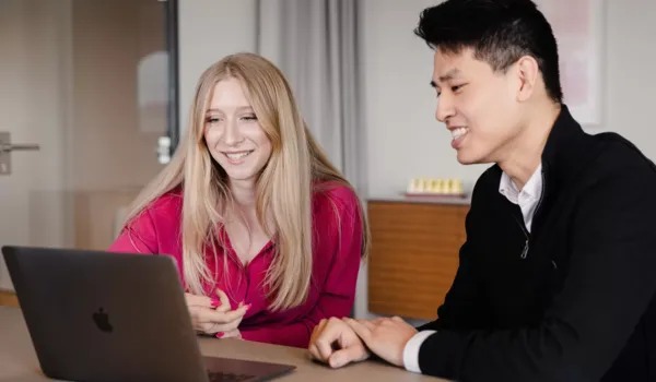 A man and a woman sitting at a table, smiling and looking at a laptop